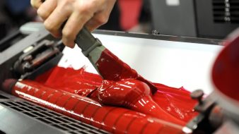 Worker uses specialized spatula to apply red paint to industrial printer